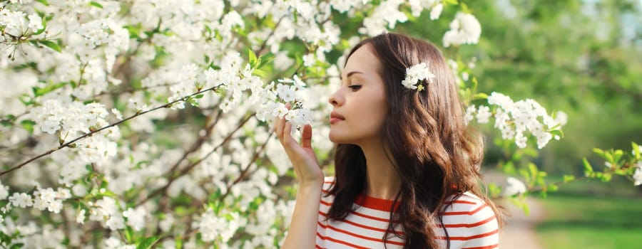 Portrait of lovely happy smiling young woman in spring blooming garden with white flowers on the trees in park