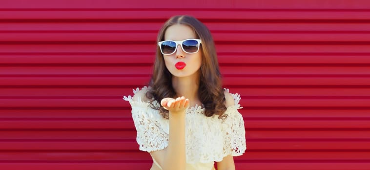 Portrait of beautiful young woman model blowing kiss wearing a white glasses posing on pink background