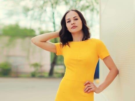 Portrait of beautiful young brunette woman model posing in yellow dress on city street