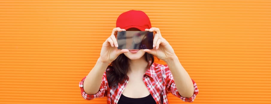 Summer portrait of happy cheerful young woman taking selfie with mobile phone on colorful orange background on city street