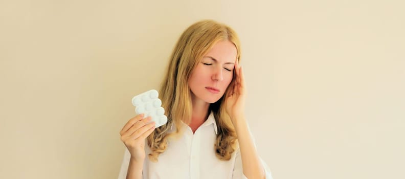 Sick exhausted young woman holding pills, tired girl suffering with headache at home