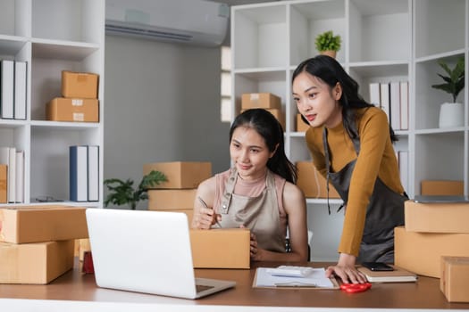 Two businesswomen managing online orders with laptop in office. Concept of e-commerce and teamwork.