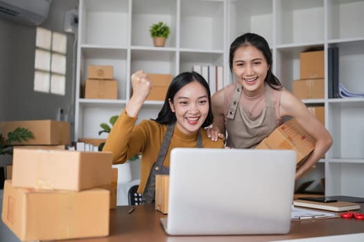 Two businesswomen celebrating online sales success in office. Concept of e-commerce and achievement.