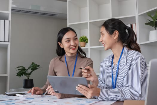 Two smiling businesswomen discussing work with tablet in modern office. Concept of teamwork and collaboration.