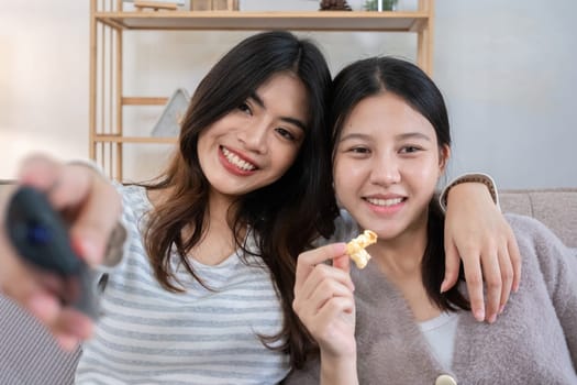 Close up two young women watching TV and eating popcorn on couch. Concept of relaxation and friendship.