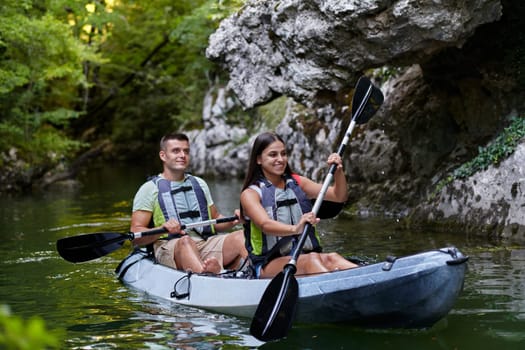 A young couple enjoying an idyllic kayak ride in the middle of a beautiful river surrounded by forest greenery.