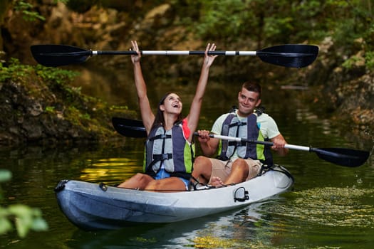 A young couple enjoying an idyllic kayak ride in the middle of a beautiful river surrounded by forest greenery.