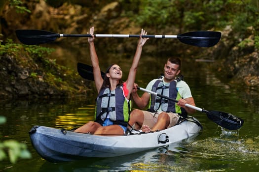 A young couple enjoying an idyllic kayak ride in the middle of a beautiful river surrounded by forest greenery.