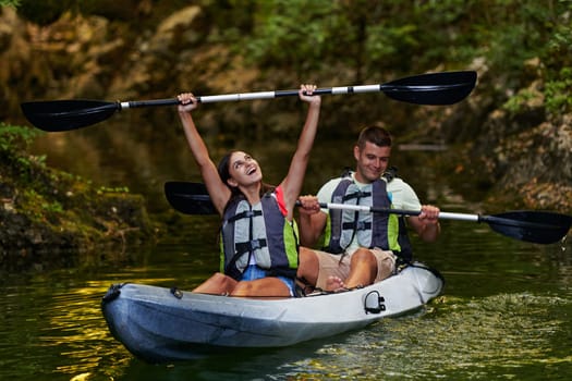 A young couple enjoying an idyllic kayak ride in the middle of a beautiful river surrounded by forest greenery.