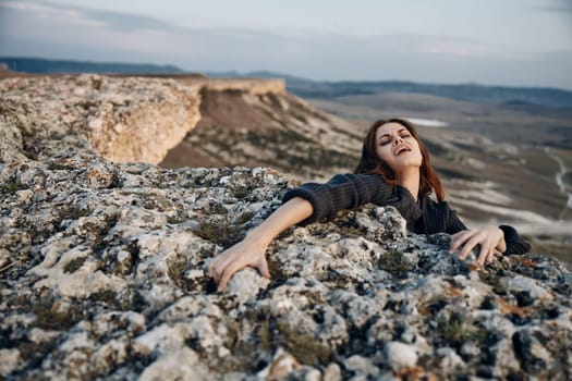 Serene woman laying on top of rock with arms outstretched and eyes closed in peaceful tranquility