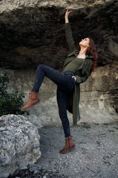 Woman standing on rock in forest wearing green coat and jeans