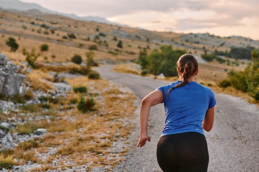 A determined female athlete runs through a forest trail at sunrise, surrounded by breathtaking natural beauty and vibrant greenery.