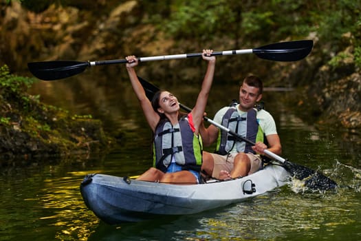 A young couple enjoying an idyllic kayak ride in the middle of a beautiful river surrounded by forest greenery.