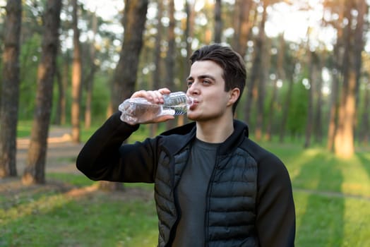 A handsome young man in a sports jacket drinking water from a bottle in nature