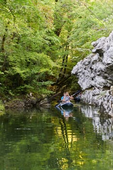 A group of friends enjoying having fun and kayaking while exploring the calm river, surrounding forest and large natural river canyons.