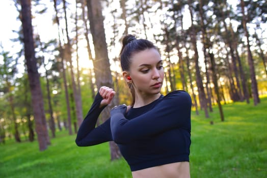 A young woman in a sporty black top is doing a workout in the forest