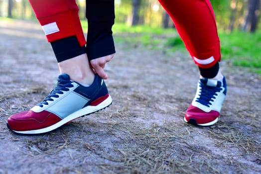 A woman on a jog in the park corrects the sneakers on her feet.