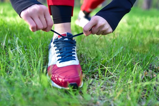 A woman ties the laces on her sneakers in the park