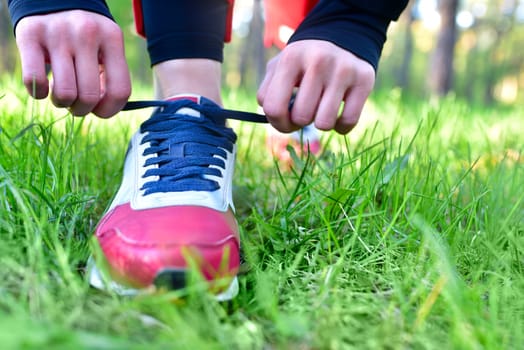 A woman tightens the laces on her athletic sneakers in a park while jogging
