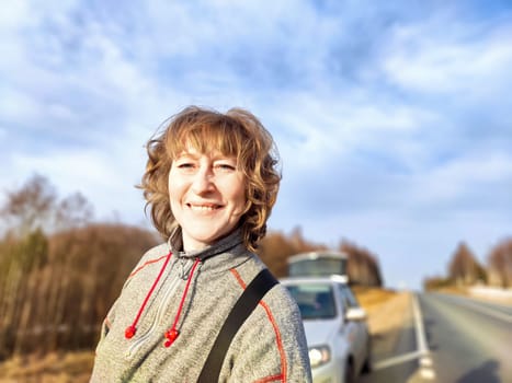 A woman takes a selfie on the road near a car. The concept of car travel. A woman captures a selfie with her car in the background during road trip