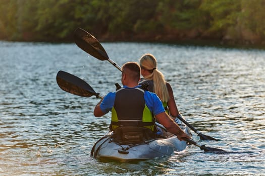 A young couple enjoying an idyllic kayak ride in the middle of a beautiful river surrounded by forest greenery in sunset time.