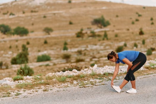 A determined female athlete stretches her muscles after a strenuous run through rugged mountain terrain, surrounded by breathtaking rocky landscapes.