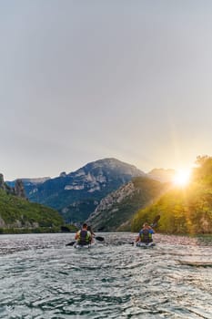 A group of friends enjoying fun and kayaking exploring the calm river, surrounding forest and large natural river canyons during an idyllic sunset