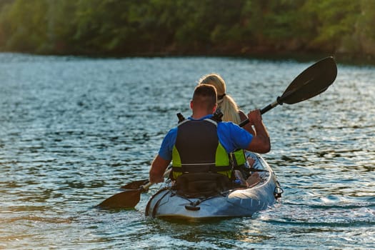 A young couple enjoying an idyllic kayak ride in the middle of a beautiful river surrounded by forest greenery in sunset time.