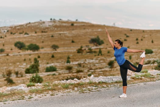 A determined female athlete stretches her muscles after a strenuous run through rugged mountain terrain, surrounded by breathtaking rocky landscapes.