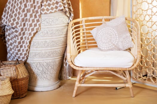 A wicker chair with a comfortable white cushion is placed beside a stylish vase, creating a cozy and inviting atmosphere. This piece of furniture combines elegance with comfort