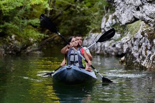 A young couple enjoying an idyllic kayak ride in the middle of a beautiful river surrounded by forest greenery.