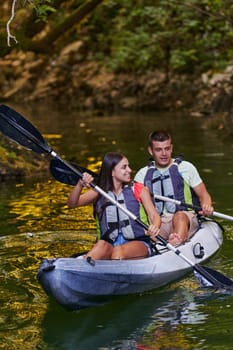 A young couple enjoying an idyllic kayak ride in the middle of a beautiful river surrounded by forest greenery.