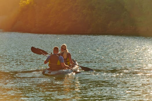 A young couple enjoying an idyllic kayak ride in the middle of a beautiful river surrounded by forest greenery in sunset time.