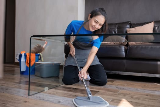 Smiling housekeeper mopping floor in living room with cleaning supplies. Concept of domestic chores and hygiene.