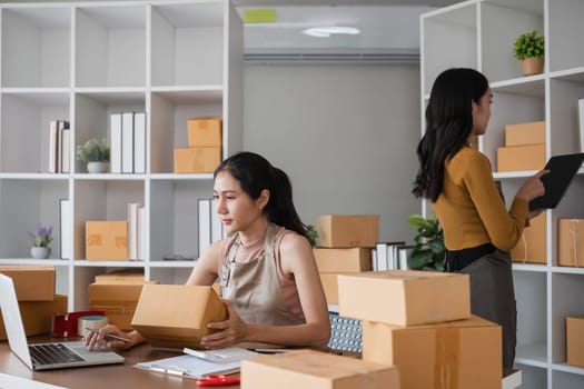 Two businesswomen organizing and preparing packages for shipping in office. Concept of e-commerce and logistics.