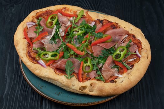 Italian Pizza on plate with jamon slices, pepper and fresh arugula leaves on top