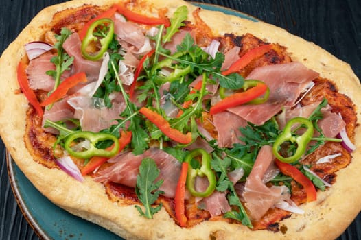 Italian Pizza on plate with jamon slices, pepper and fresh arugula leaves on top