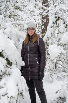 Woman in winter jacket walking in snowy winter forest, snowy winter day