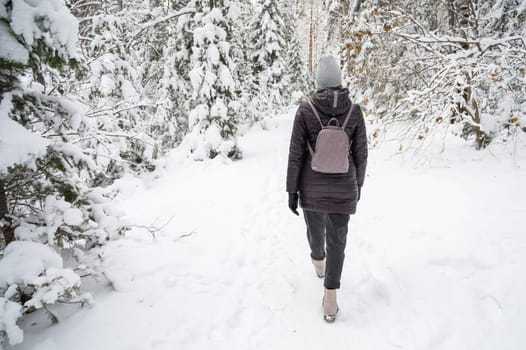 Woman in winter jacket walking in snowy winter forest, snowy winter day