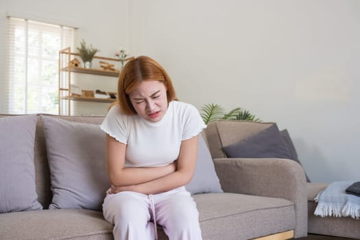 Young Asian Woman Suffering from Stomach Pain on Sofa.