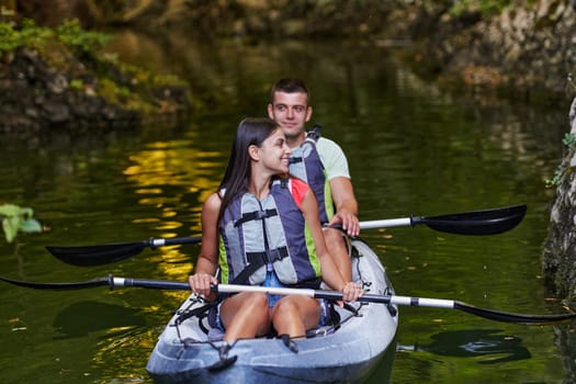 A young couple enjoying an idyllic kayak ride in the middle of a beautiful river surrounded by forest greenery.