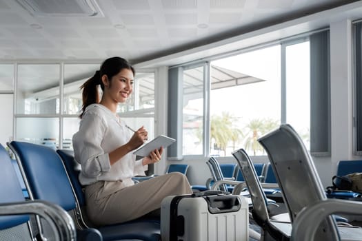 Young woman waiting at airport with luggage and tablet. Concept of travel and technology.