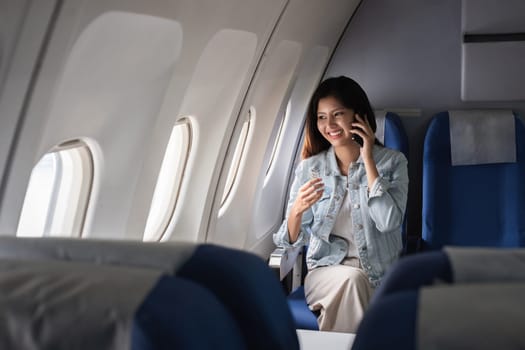 Young woman talking on smartphone during flight on airplane. Concept of travel and communication.