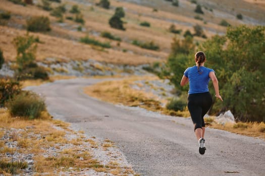 A determined female athlete runs through a forest trail at sunrise, surrounded by breathtaking natural beauty and vibrant greenery.