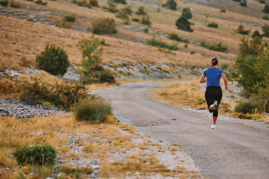 A determined female athlete runs through a forest trail at sunrise, surrounded by breathtaking natural beauty and vibrant greenery.