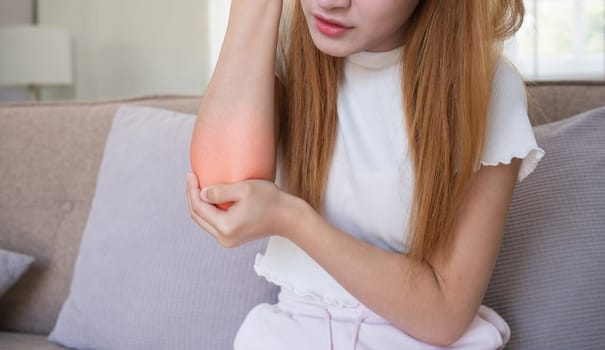 Close up Asian woman suffering from elbow pain at home. Concept of physical discomfort, pain relief, and health issues.