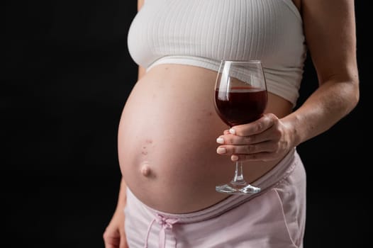 Close-up of the belly of a pregnant woman holding a glass of red wine while sitting on the sofa. Copy space