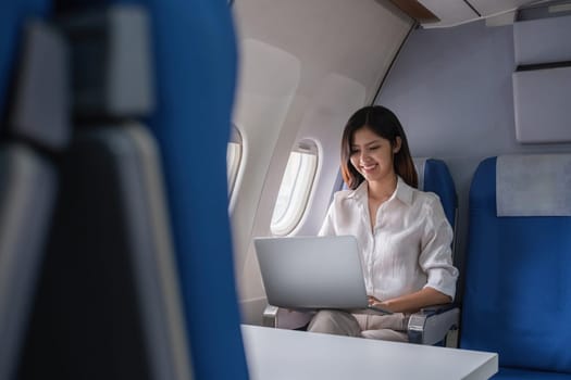 Young woman working on laptop during flight on airplane. Concept of travel and remote work.