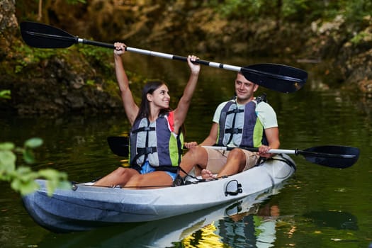 A young couple enjoying an idyllic kayak ride in the middle of a beautiful river surrounded by forest greenery.