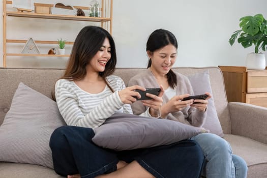 Two young women playing games on smartphones together at home. Concept of friendship and technology.